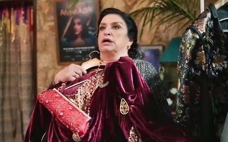 A atriz Grace Gianoukas segura um cabide com vestido e bolsa em cena da novela Terra e Paixão como uma atriz