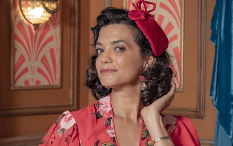 Ana Cecília Costa está caracterizada como Verônica com figurino vermelho em um cenário da novela Amor Perfeito, da Globo