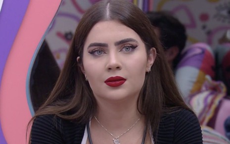 A participante do BBB 22 Jade Picon olha séria enquanto está sentada no quarto Lollipop do reality da Globo