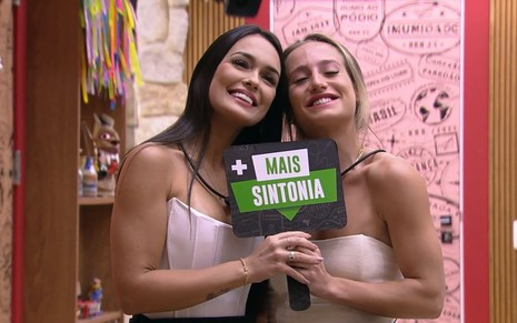 Larissa Santos e Bruna Griphao seguram placa escrito 'mais sintonia', no BBB 23