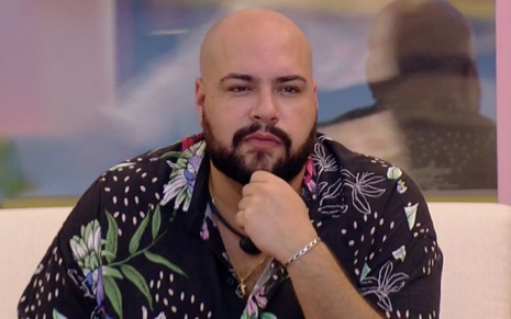 O participante do BBB22 Tiago Abravanel olha pensativo sentado na área externa do reality da Globo