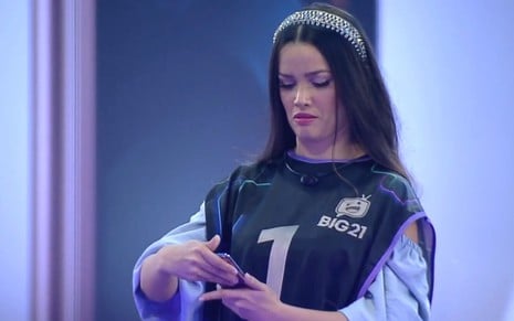 Com colete preto, Juliette Freire abre celular em ação de merchandising no Big Brother Brasil, da Globo