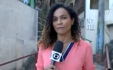 A repórter Daniela Carla, da TV Gazeta, com uma camisa rosa e segurando um microfone com o logo da Globo