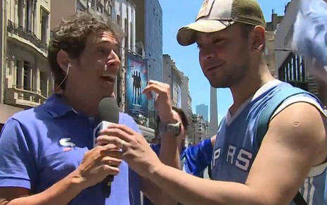 Bruno Côrtes segura o microfone da Globo junto com um torcedor da Argentina