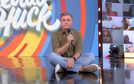 Luciano Huck está sentado no estúdio do Caldeirão do Huck, da Globo