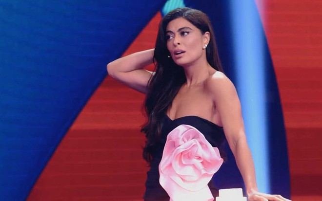 A atriz Juliana Paes leva a mão direita à cabeça e faz cara de confusa no palco do Caldeirão