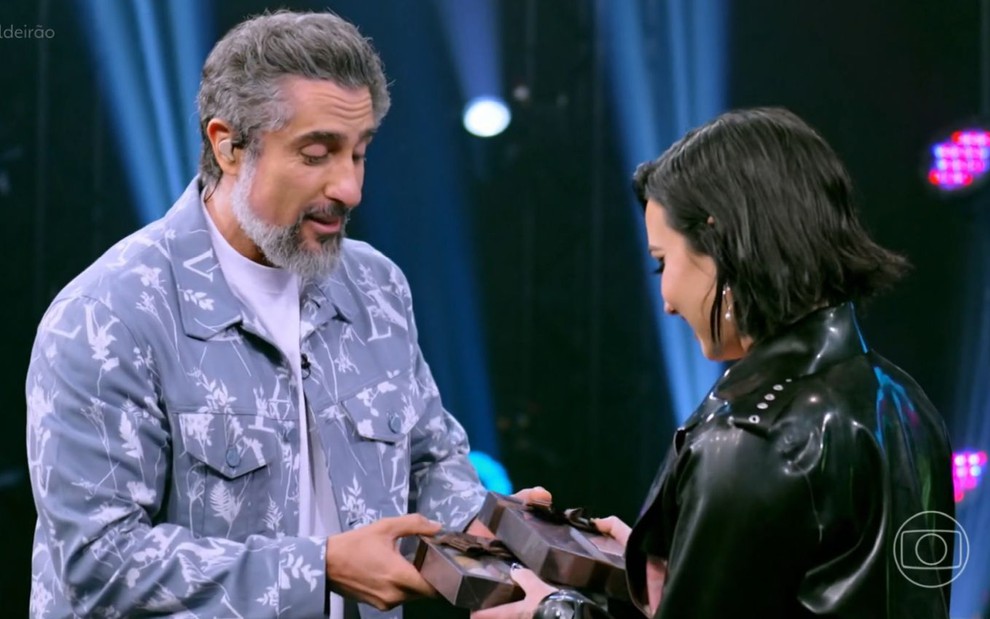 Marcos Mion entrega caixas para Demi Lovato no cenário do Caldeirão