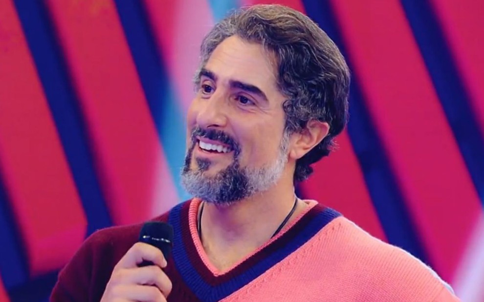 O apresentador Marcos Mion sorri feliz segurando um microfone no programa Caldeirão exibido no sábado (4) na Globo