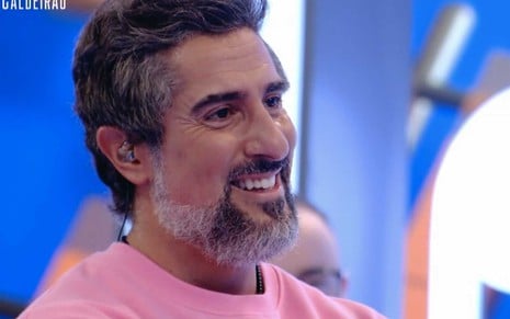 O apresentador Marcos Mion visivelmente emocionado com um moleton rosa, de perfil, no palco do Caldeirão
