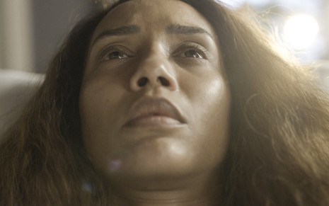 A atriz Taís Araujo olha para cima em gravação de cena de Cara e Coragem na qual ela está sem maquiagem e com cabelos soltos