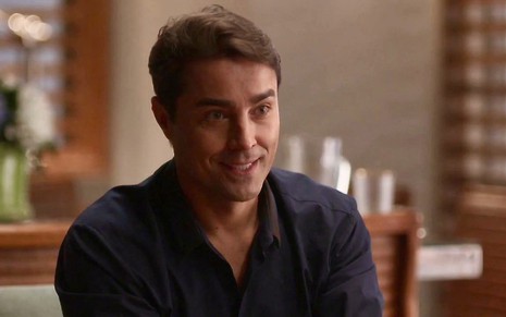 O ator Ricardo Pereira está com um sorriso estranho  em cena da novela Cara e Coragem na qual usa camisa preta