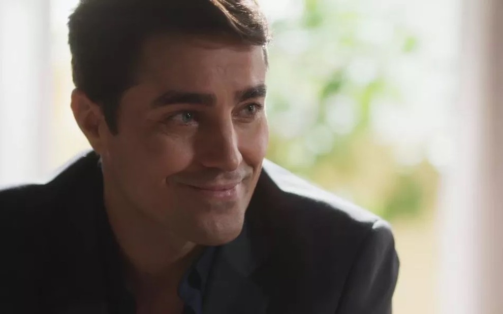 O ator Ricardo Pereira usa terno preto em cena de Cara e Coragem e dá um sorriso sarcástico ao interpretar o vilão Danilo