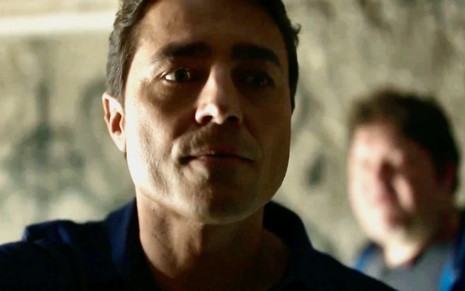 O ator Ricardo Pereira está em close como o personagem Danilo em cena de Cara e Coragem, e Adriano Petterman aparece ao fundo desfocado