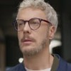 Guilherme Weber caracterizado como Jonathan; ator tem os cabelos loiros e usa um óculos com armação preta em cena de Cara e Coragem