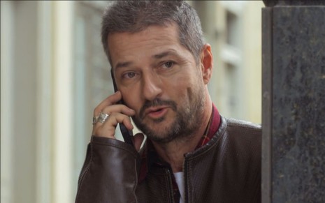 Marcelo Serrado grava cena ao telefone, com expressão séria, como Moa em Cara e Coragem