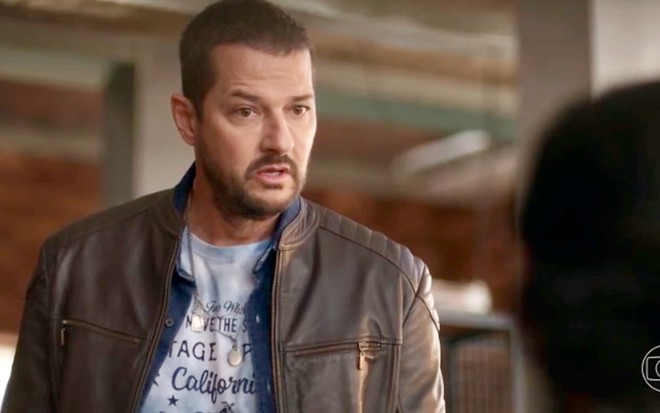 O ator Marcelo Serrado encara alguém que não aparece na imagem em cena de Cara e Coragem, na qual usa camiseta e jaqueta