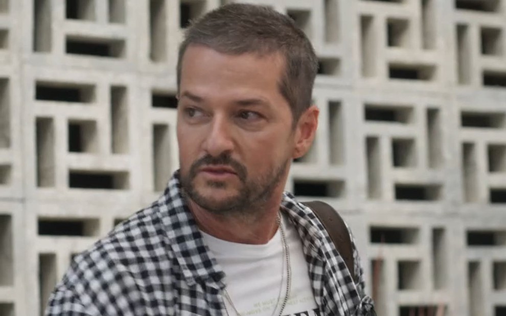 Marcelo Serrado, caracterizado como Moa, usa blusa branca e camisa xadrez preta e branca. Ele tem a expressão assustada em cena de Cara e Coragem