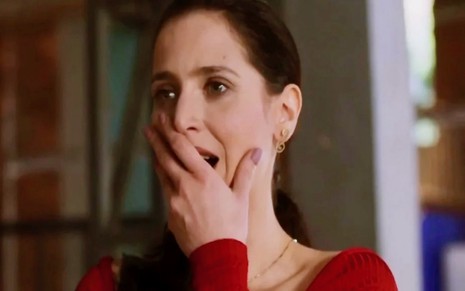 A atriz Mel Lisboa em cena de Cara e Coragem na qual usa uma blusa vermelha de manga longa e coloca a mão na boca