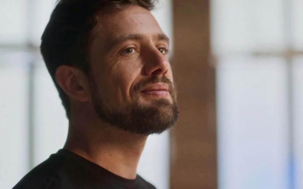 O ator Rafael Cardoso usa camiseta preta e está em close em cena da novela das sete da Globo, Cara e Coragem