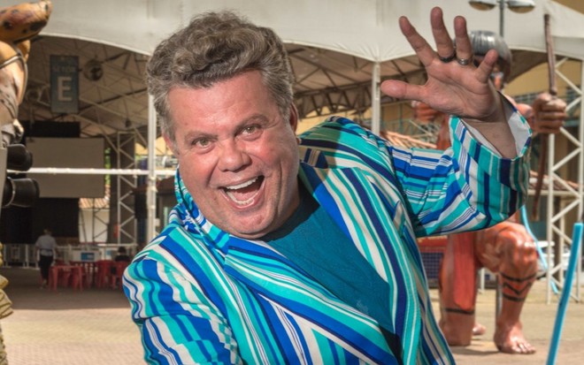 Milton Cunha sorri em ensaio do Carnaval da Globo; ele está de terno azul com listras