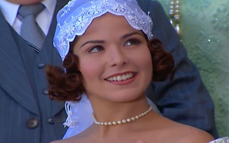 Samara Felippo, caracterizada como Celina, em cena de Chocolate com Pimenta; atriz usa vestido de noiva, com véu no estilo da década 1920, e sorri