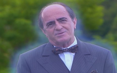 Ary Fontoura caracterizado como Ludovico; ele usa um terno cinza e sorri. Sua imagem está levemente transparente em cena de Chocolate com Pimenta