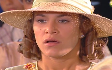 Priscila Fantin caracterizada como Olga; ela usa um vestido rosa e cabelo cacheado na altura dos ombros em cena de Chocolate com Pimenta
