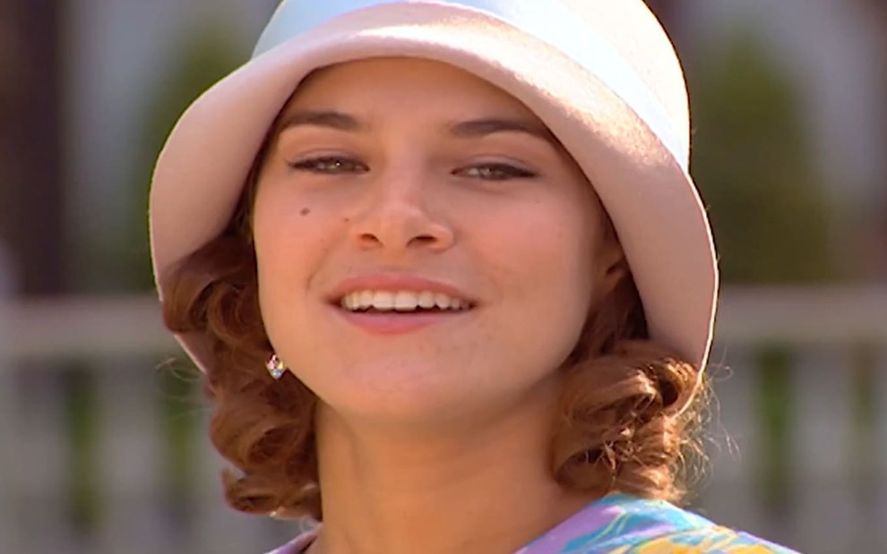 Priscila Fantin caracterizada como Olga; ela usa um vestido roxo e tem o cabelo cacheado na altura dos ombros em cena de Chocolate com Pimenta. O semblante exprime raiva.