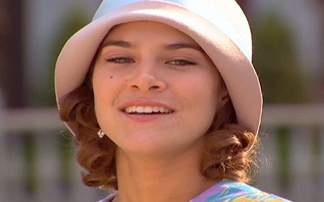 Priscila Fantin caracterizada como Olga; ela usa um vestido roxo e tem o cabelo cacheado na altura dos ombros em cena de Chocolate com Pimenta. O semblante exprime raiva.