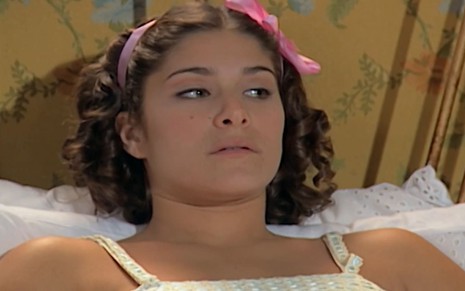 Priscila Fantin, caracterizada como Olga, tem a expressão falsamente debilitada em cena de Chocolate com Pimenta; ela usa uma camisola branca, e um laço rosa
