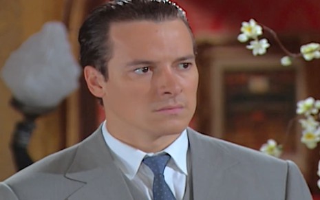 Rodrigo Faro caracterizado como Guilherme; ele usa um terno cinza e tem o semblante sério em cena de Chocolate com Pimenta