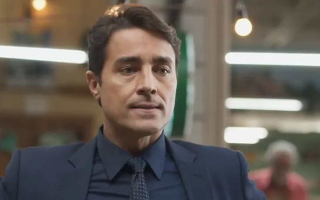 O ator Ricardo Pereira usa terno, camisa e gravata escuros e faz expressão de raiva em cena de Cara e Coragem, novela das sete da Globo
