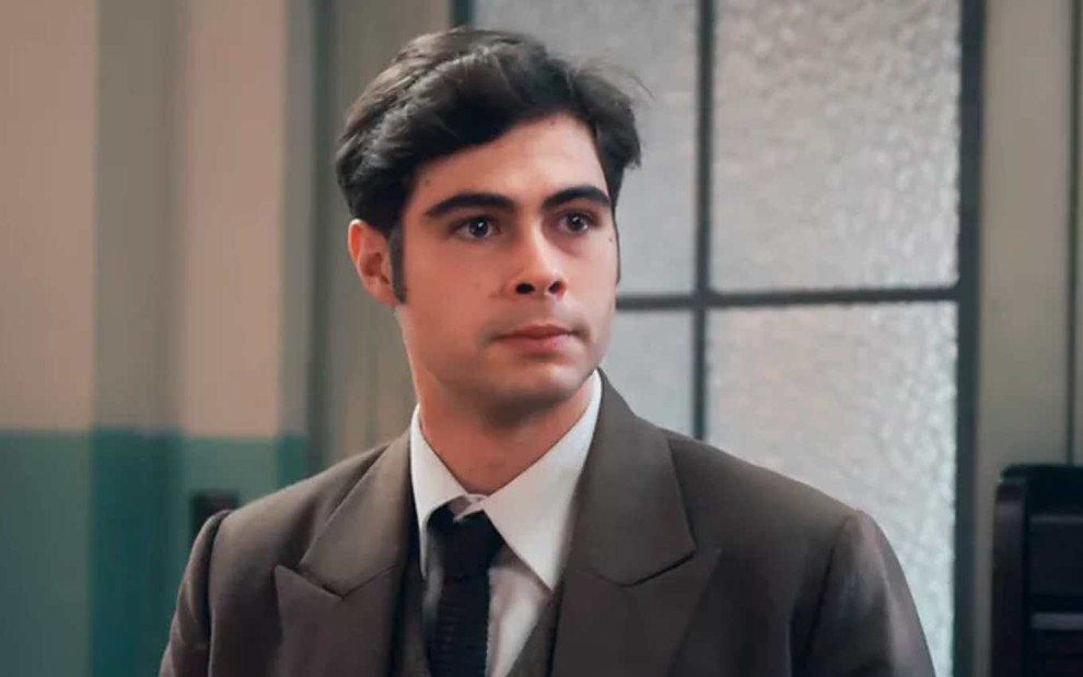 O ator Rafael Vitti de terno e gravata, com expressão séria em cena de Além da Ilusão