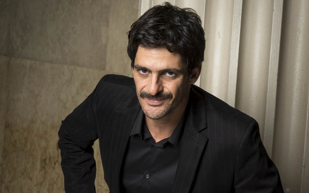 O ator Julio Machado, de terno preto e bigode, posando para foto