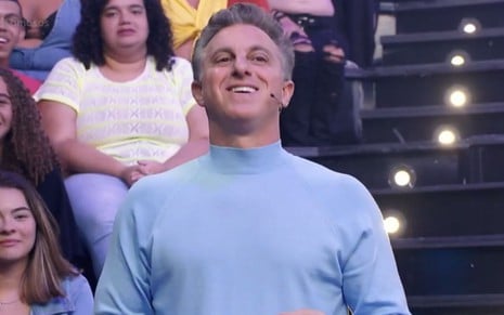 Luciano Huck sorri e usa uma blusa azul enquanto comando o Domingão na Globo