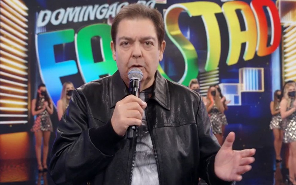 Fausto Silva com uma jaqueta preta, no comando de seu antigo programa dominical na Globo
