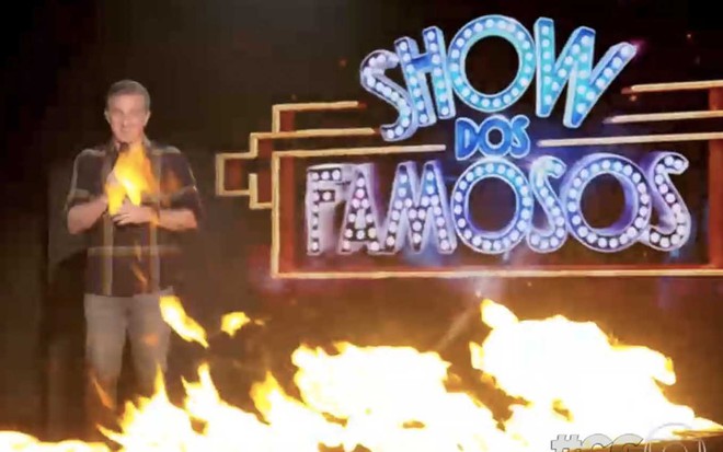 Luciano Huck no palco do Domingão com fogo criado por computação gráfica diante do letreiro do Show dos Famosos