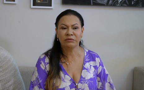 Dona Ruth Dias veste uma blusa florida e tem expressão de tristeza
