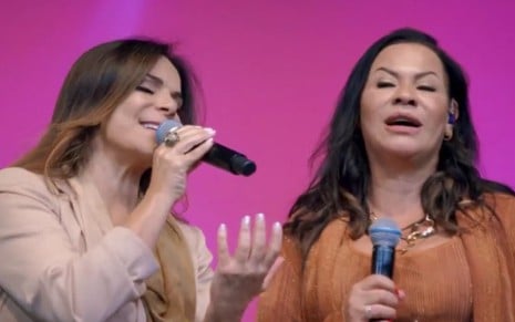 Sula Miranda e Ruth Dias estão no palco, segurando microfones, de olhos fechados