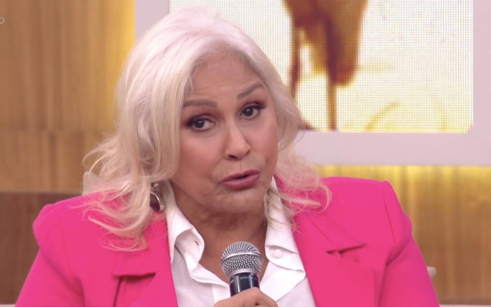 A cantora Fafá de Belém no sofá do Encontro com um terno rosa e um microfone na mão