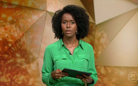 De camisa verde, Maria Júlia segura um tablet e discursa no Fantástico de 12 de dezembro