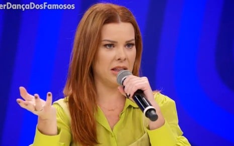 De amarelo, Fernanda Souza fala ao microfone no júri da Super Dança dos Famosos