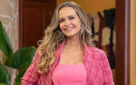 A atriz Fernanda Rodrigues de blusa e jaqueta rosas, sorrindo, caracterizada como sua personagem em Fuzuê