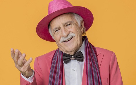 Ary Fontoura está caracterizado como Lampião/Lumière, de Fuzuê; ele usa chapéu e terno rosa e gravata borboleta