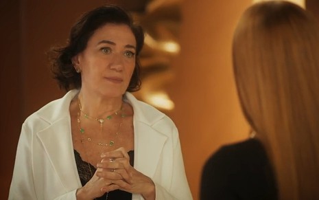 Bebel (Lilia Cabral) com expressão séria diante de Preciosa (Marina Ruy Barbosa), de costas em cena de Fuzuê