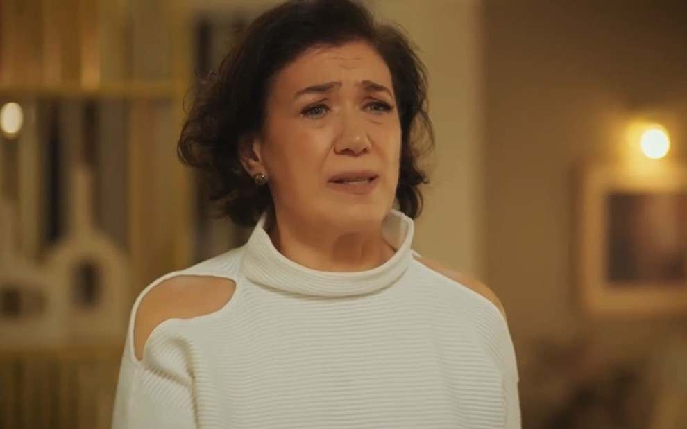 Lilia Cabral caracterizada como Bebel; ela usa uma blusa branca em cena de Fuzuê; atriz exprime preocupação.