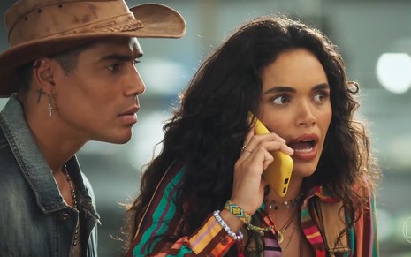 Micael Borges observa Giovana Cordeiro, que tem expressão de choque enquanto fala no celular, em cena de Fuzuê
