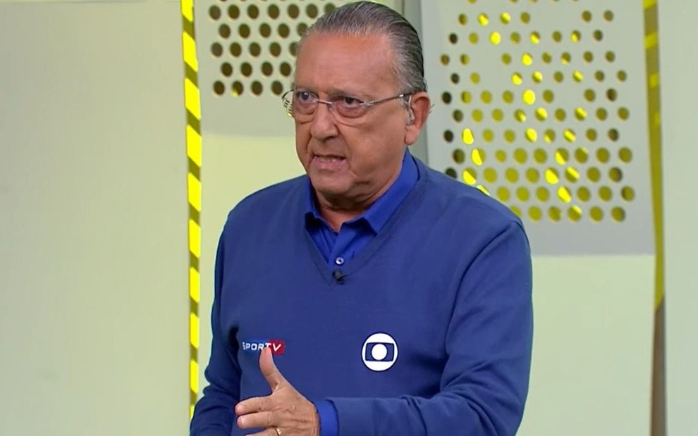 Galvão Bueno com uma blusa azul e calça marrom, no estúdio da Globo em São Paulo