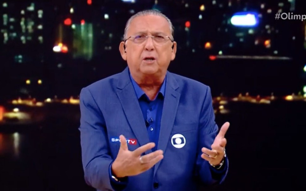Galvão Bueno em cerimônia de encerramento dos Jogos Olímpicos: narrador usa camisa e terno azul com o logo do Globo, gesticula com as mãos e tem expressão séria