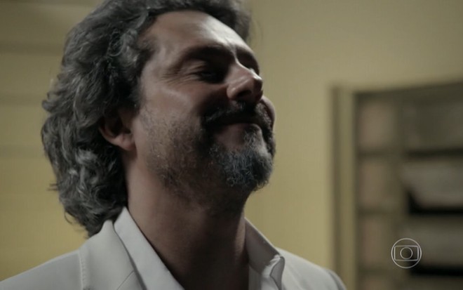 Alexsndre Nero sorri com os olhos fechados em cena como o comendador da novela Império